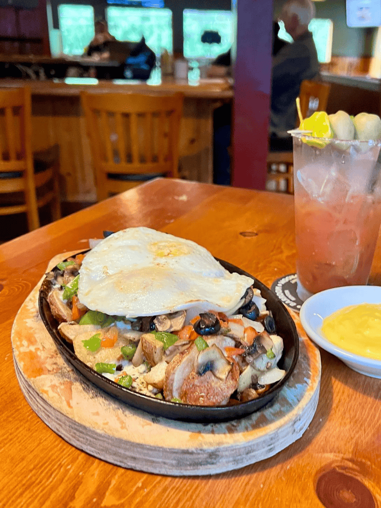 Savory skillet dish topped with fried egg, served with lemon drink and mustard sauce in cozy restaurant.