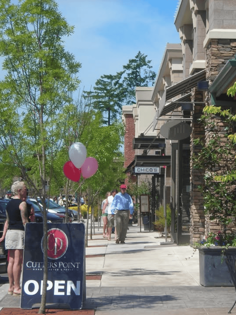 Outdoor shopping street with cafes and boutiques, surrounded by trees and modern architecture.