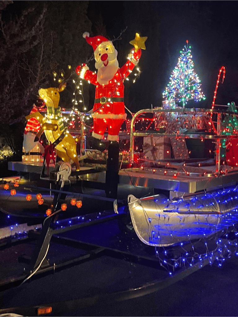 Santa Claus with reindeer Christmas float decorated with colorful lights and a Christmas tree in the background.