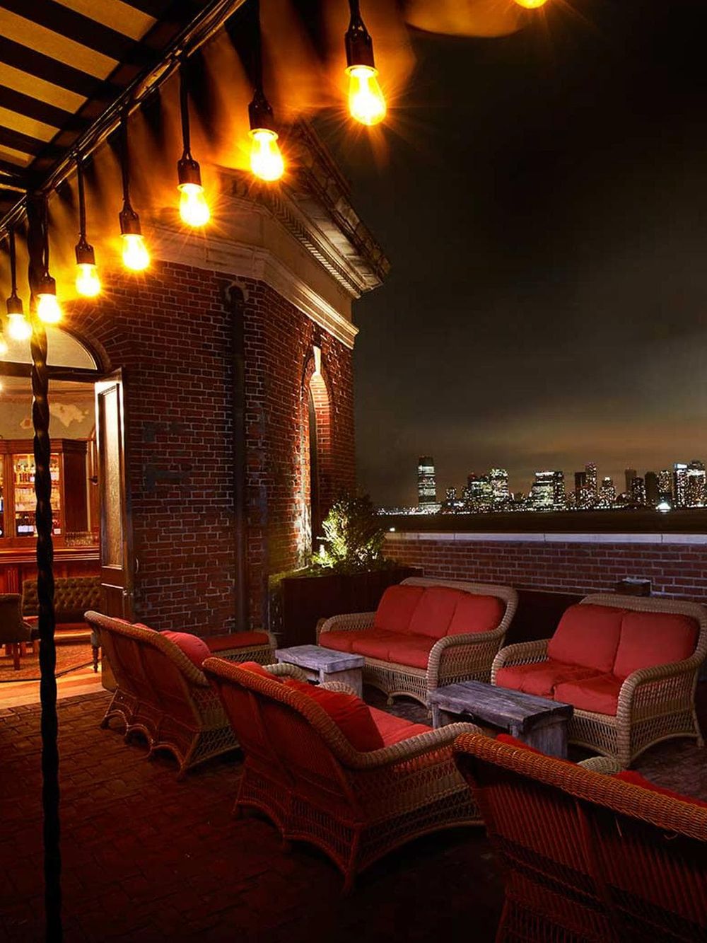 Warm ambient lighting on a cozy rooftop lounge with a city skyline view at night.
