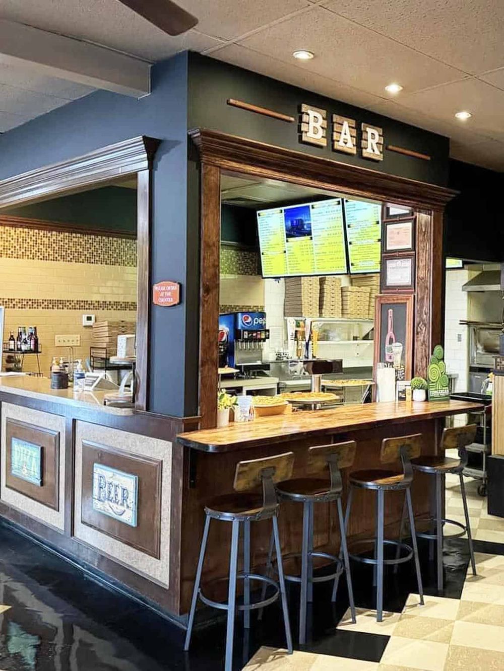 Cozy bar area inside a restaurant with a wooden counter, stools, and digital menu boards.