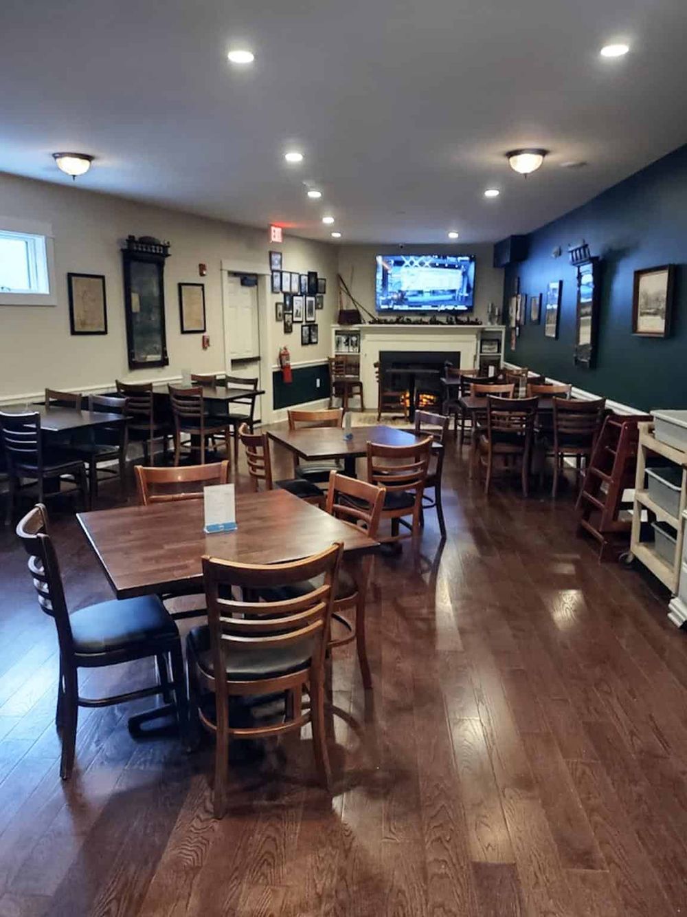 Cozy restaurant interior with wooden tables, chairs, and a fireplace, perfect for dining and social gatherings.