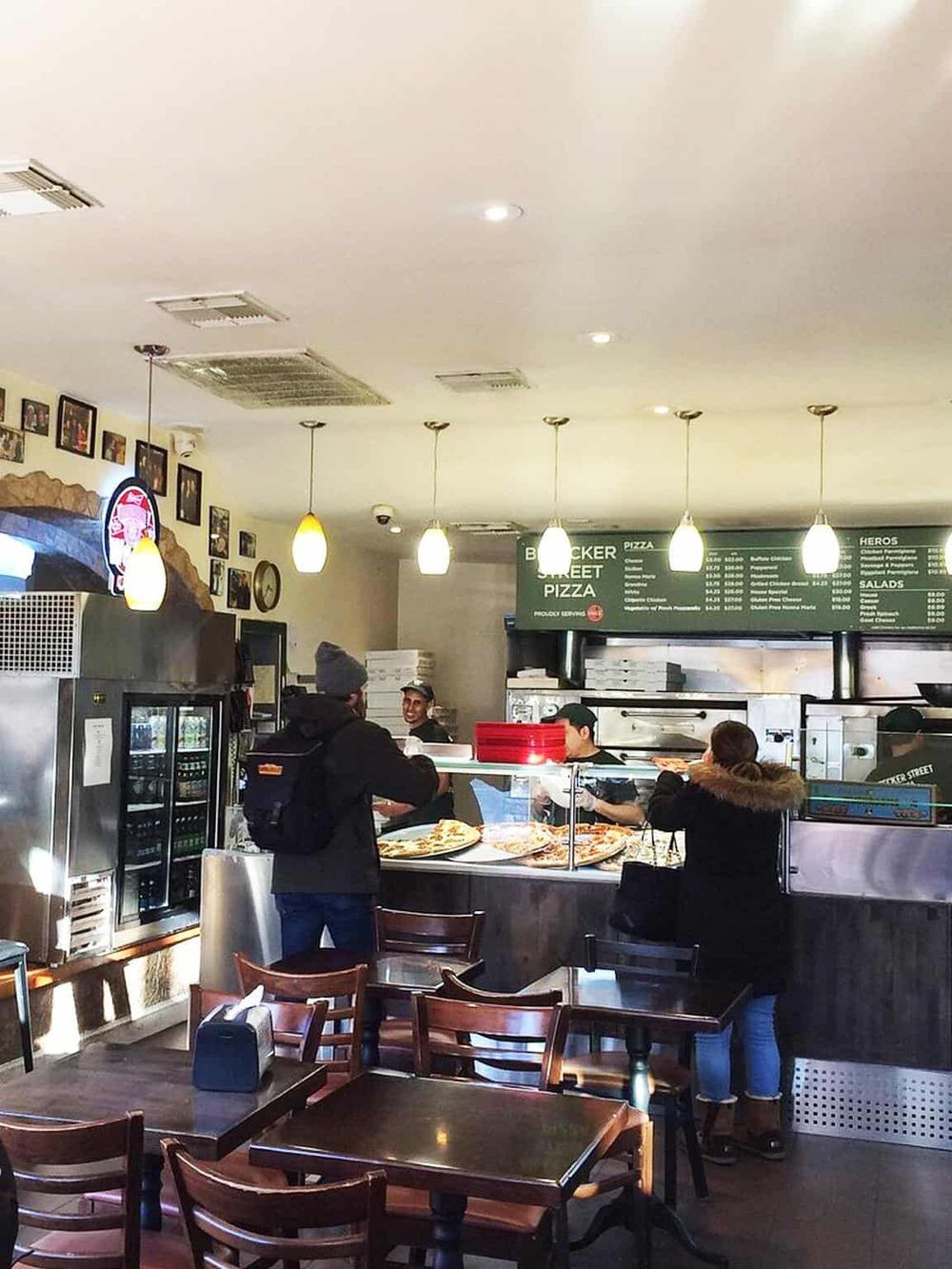 Cozy pizza restaurant interior with customers ordering, menu board, and warm lighting.