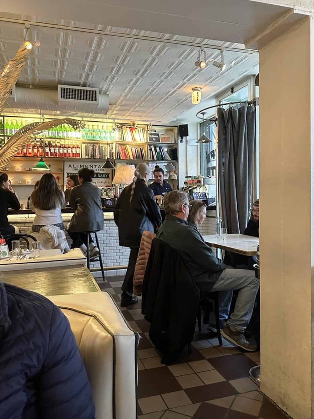 Cozy urban café interior with customers, barista, bookshelves, and modern décor.