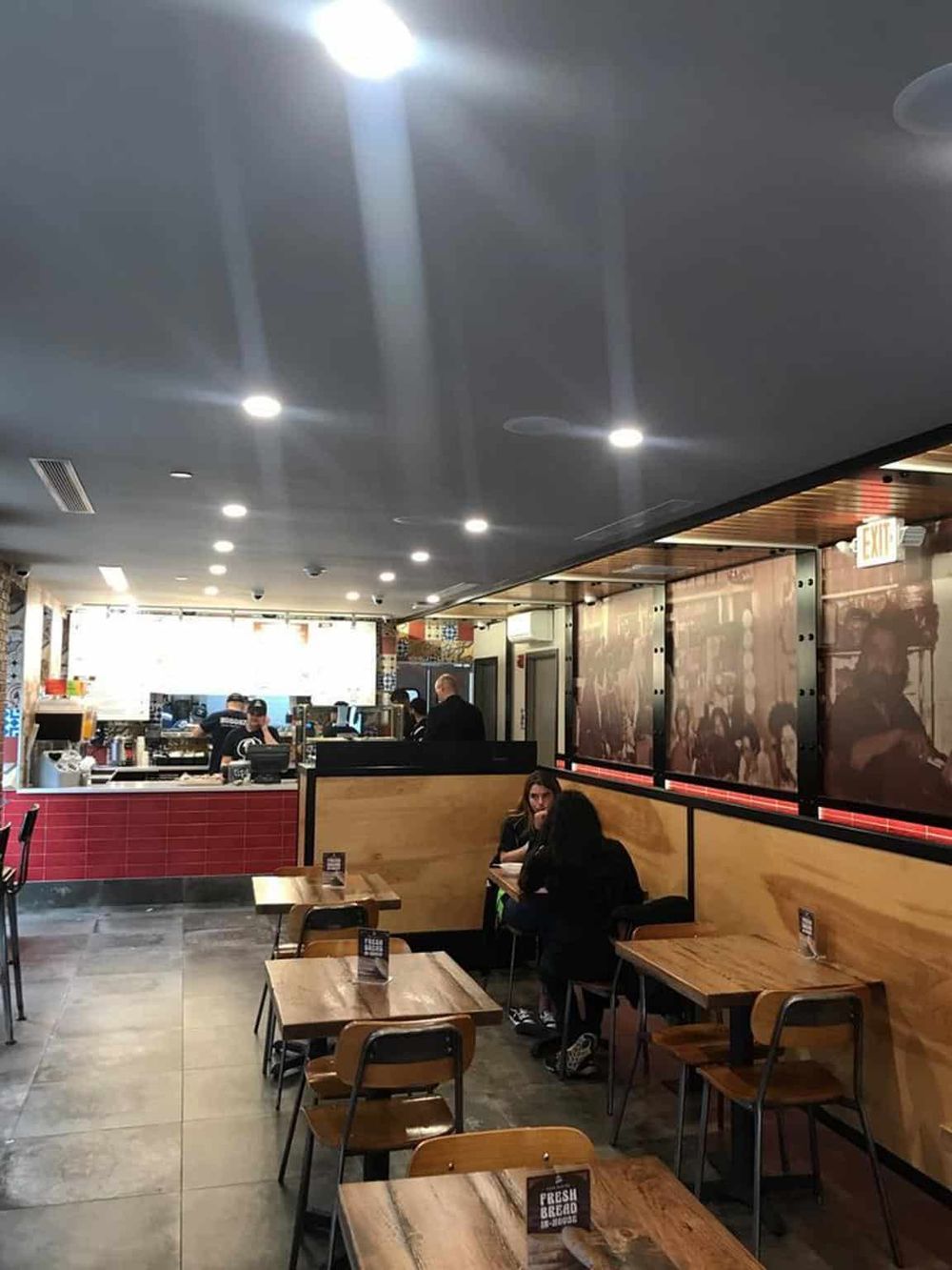 Cozy fast-casual restaurant interior with wooden tables, booth seating, and a visible open kitchen area.
