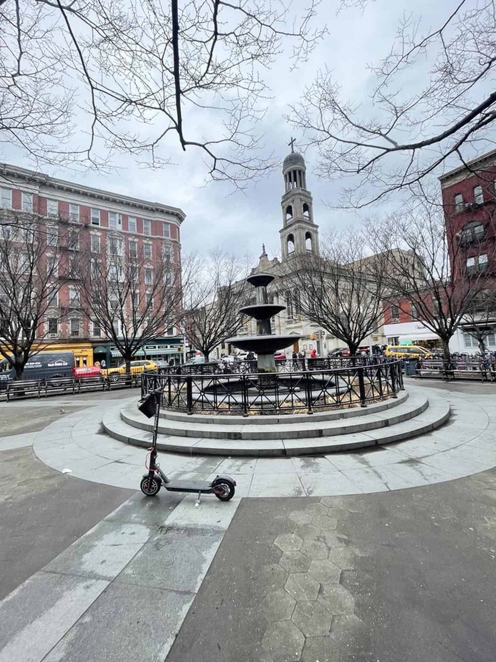 Urban city square with fountain and historic church, surrounded by trees and buildings, perfect for local exploration.