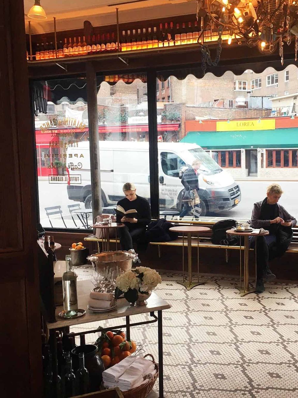Cozy coffee shop interior with large front window, showcasing customers enjoying their drinks and reading. Stylish decor enhances the inviting atmosphere.