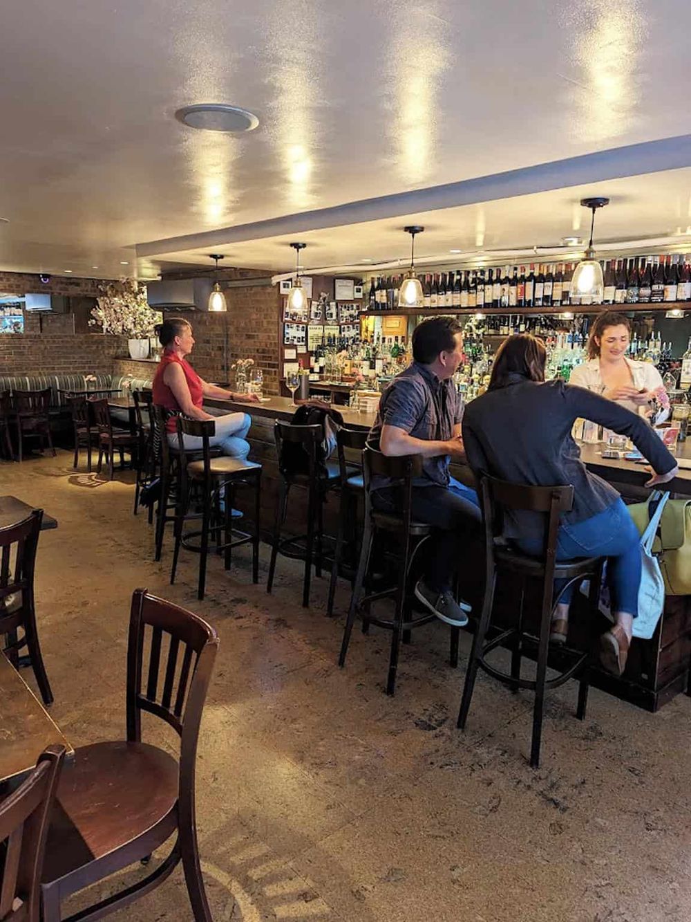 Cozy bar interior with customers enjoying drinks at the counter, warm lighting, and wine bottles on shelves, perfect for socializing.