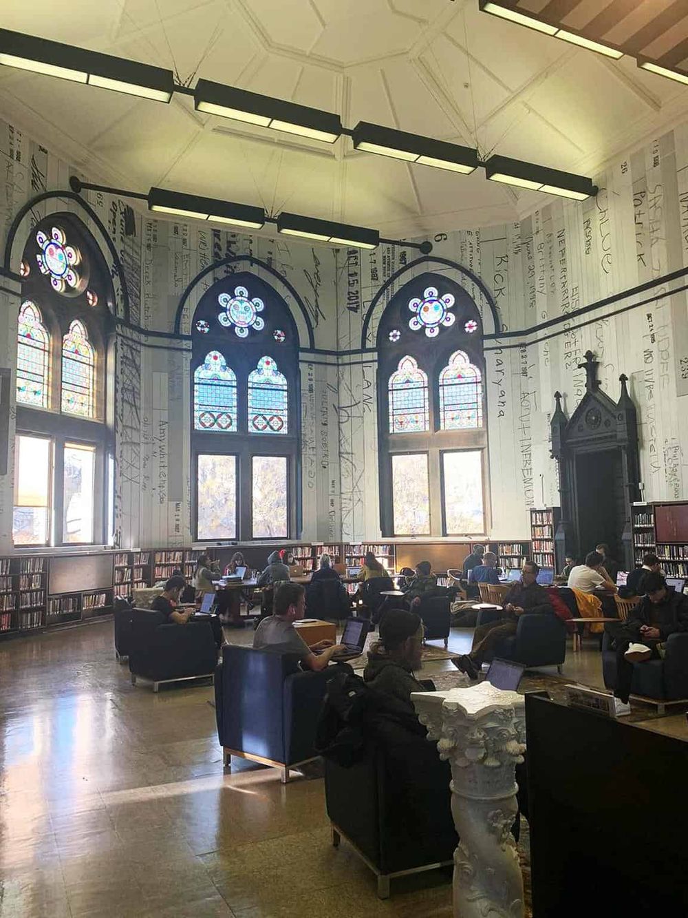 Bright library with stained glass windows and students working on laptops, fostering a conducive study environment.