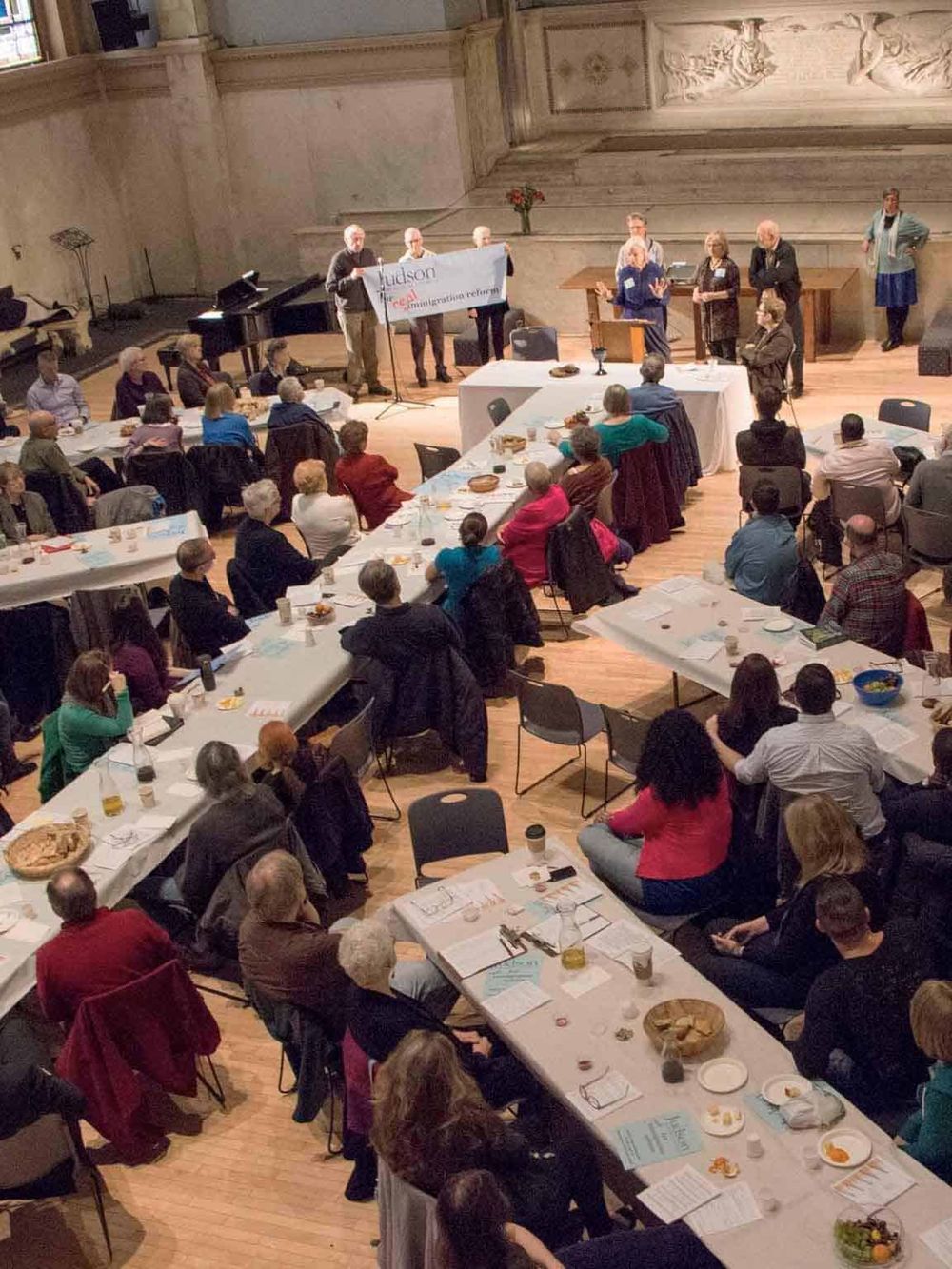 Diverse group of people attending a community event or meeting in a historic hall with classic architecture.