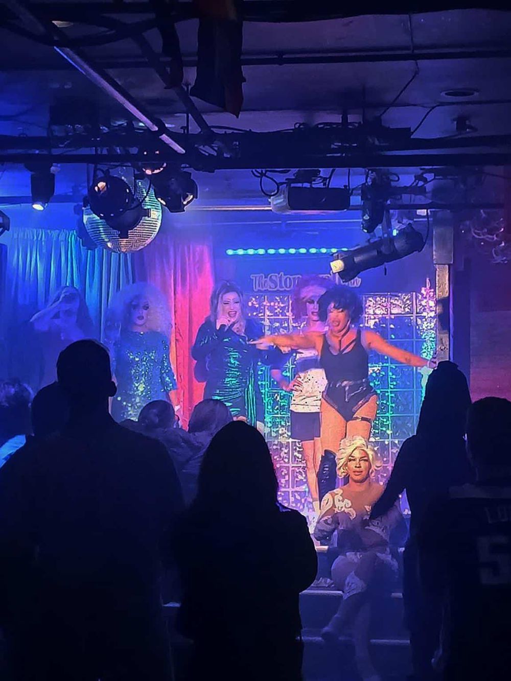 Drag Queen performance at a lively nightclub, vibrant lights, and a dynamic atmosphere.