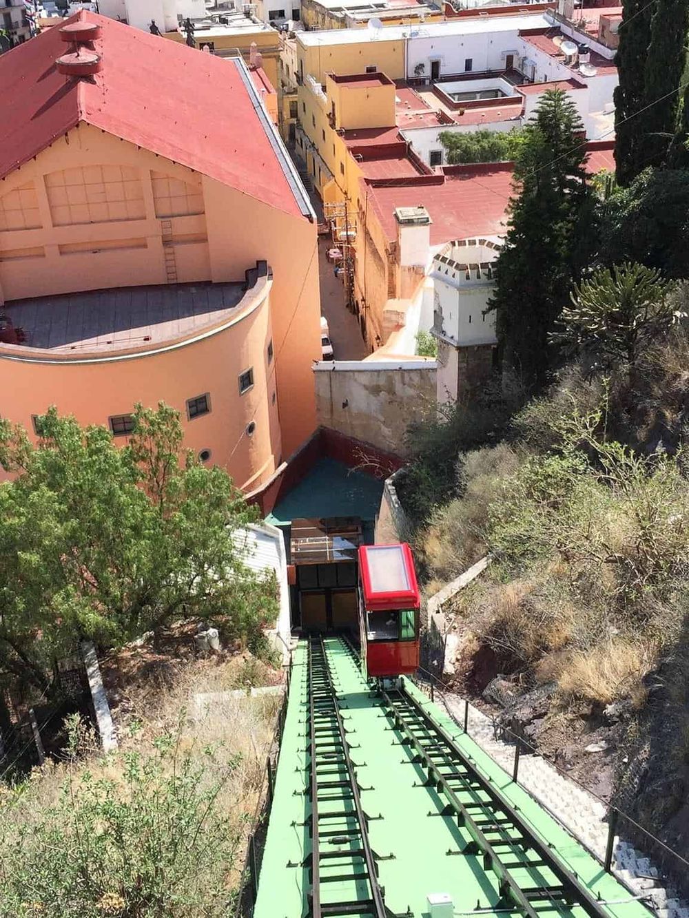 Red funicular tram ascending hillside amid colorful buildings in Mexico City.