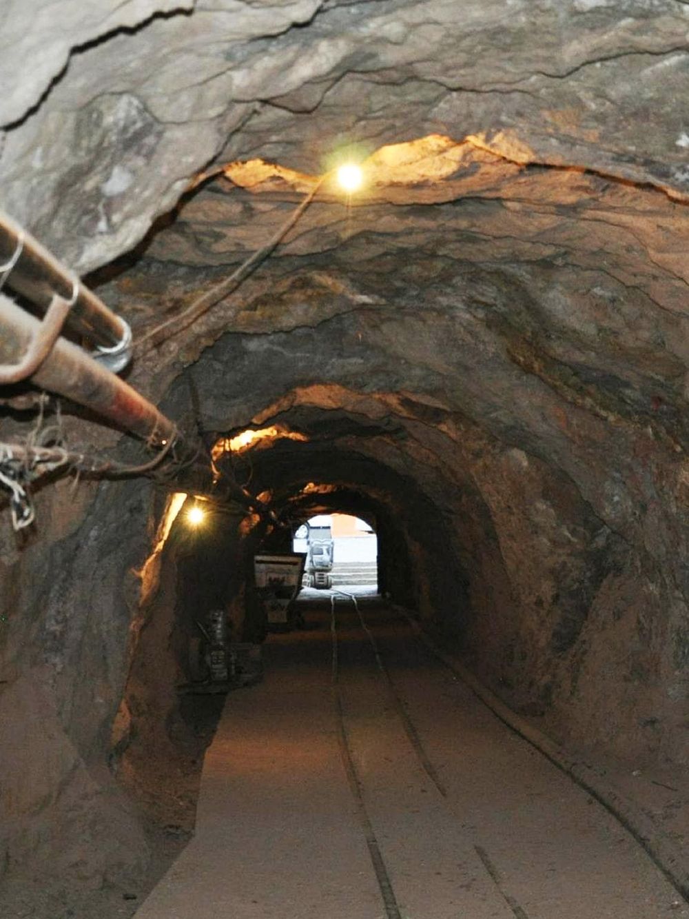 Underground mine tunnel with track, safety lighting, and construction equipment.