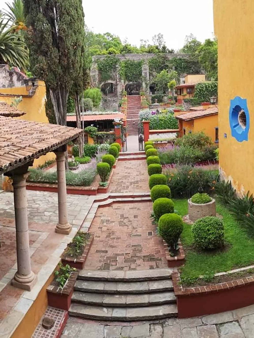 Colorful Mediterranean courtyard with lush greenery, stone pathways, and garden terraces.