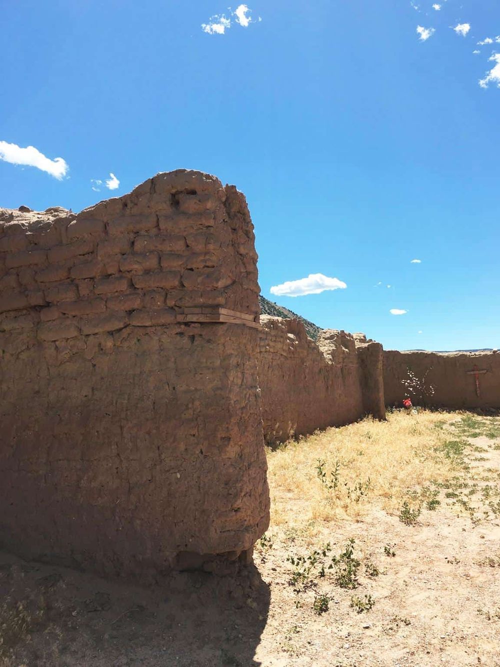 Ancient adobe ruins in New Mexico under a bright blue sky with clouds.