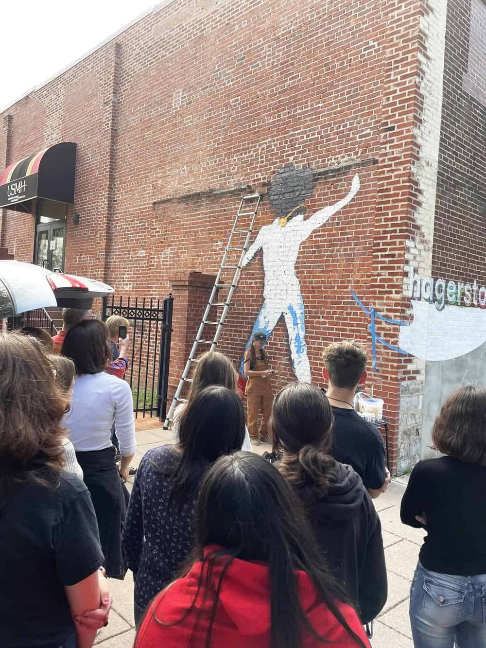 Vibrant mural painting on brick wall showcasing a woman with natural hair, engaging community in urban art event.