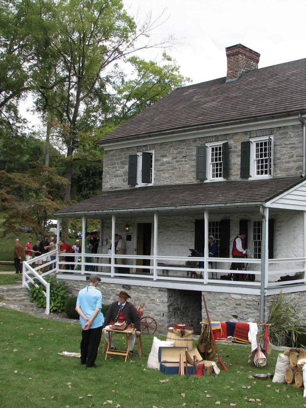Historic stone house with a porch, people dressed in period costumes, and a reenactment scene.