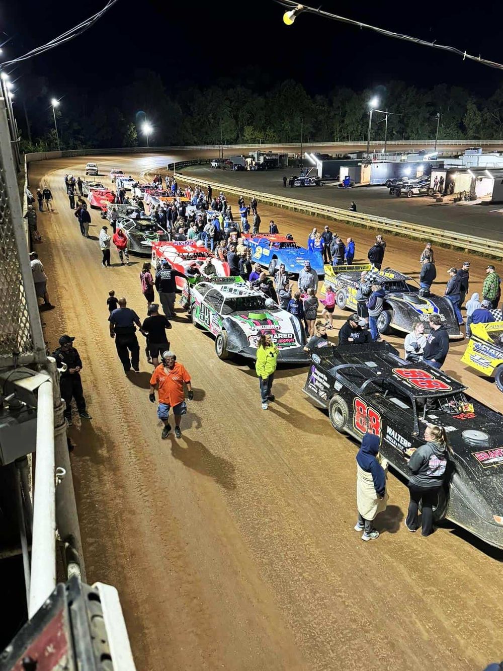 Colorful race cars lined up at a dirt track with spectators and race officials, nighttime racing event at QuestForDirections.