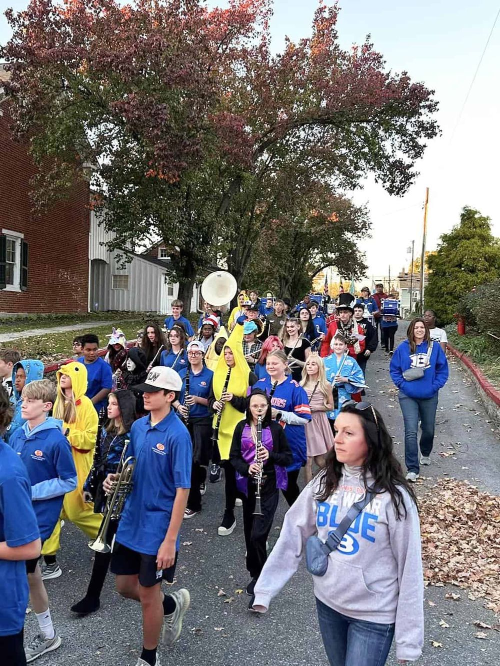 Children's marching band parade on a fall afternoon with colorful trees and town street scenery.