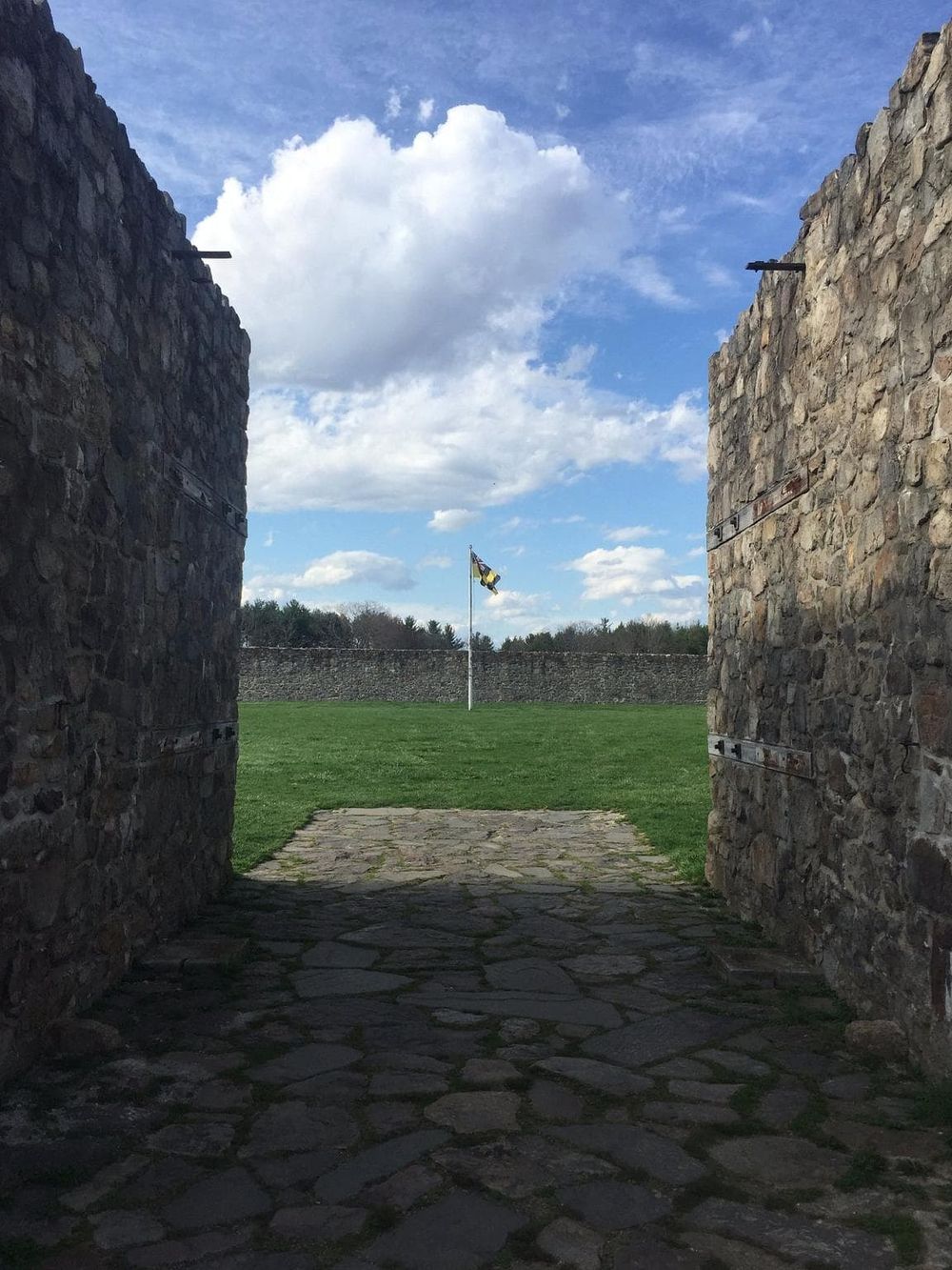 Stone gate opening at historic battle site with flag in distance, scenic outdoor travel destination.