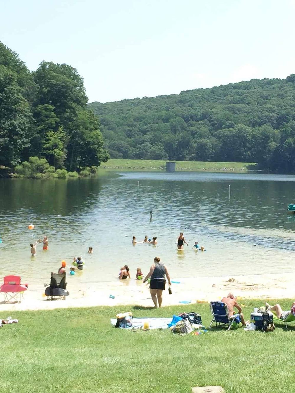 Tranquil lake swimming area with families, surrounded by lush greenery and forested hills.