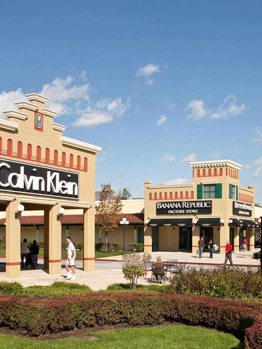 Bright shopping mall exterior with stores like Banana Republic and McKen under clear blue sky.