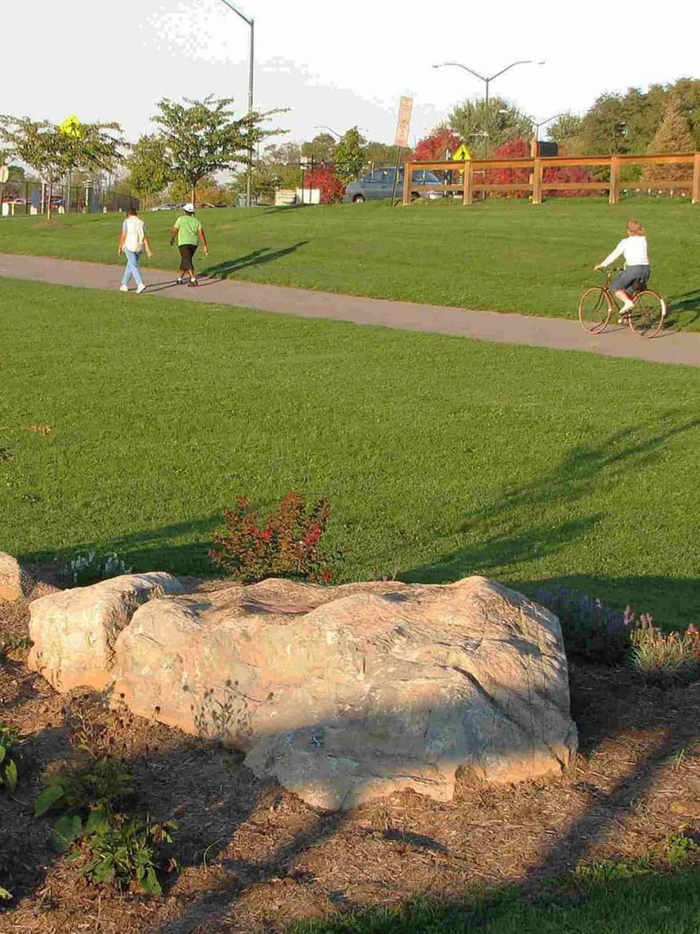 Kids walking and biking in a park with green grass and trees.