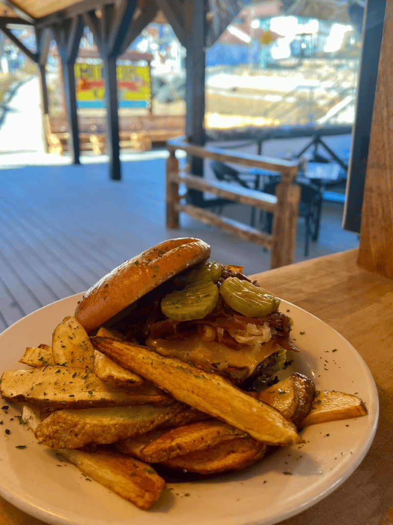 Juicy burger with pickles and crispy potato fries at outdoor restaurant setting.