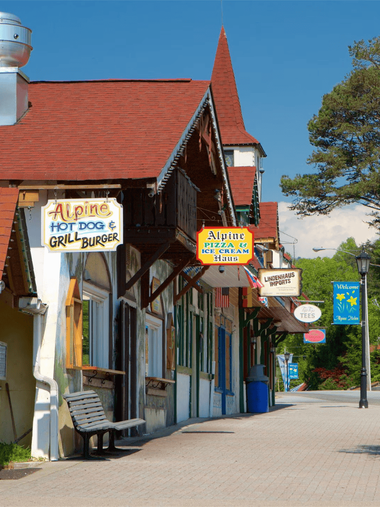 Alpine town street with shops and colorful signs for hot dogs, pizza, ice cream, and souvenirs.