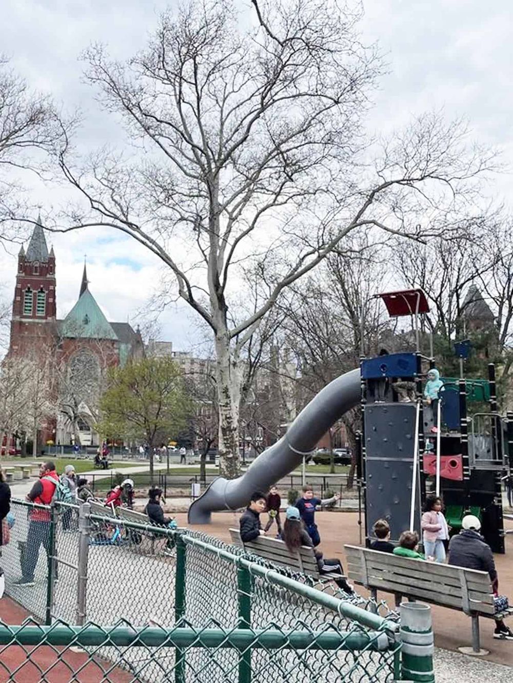 Colorful playground slide and children at park with historic church in background.