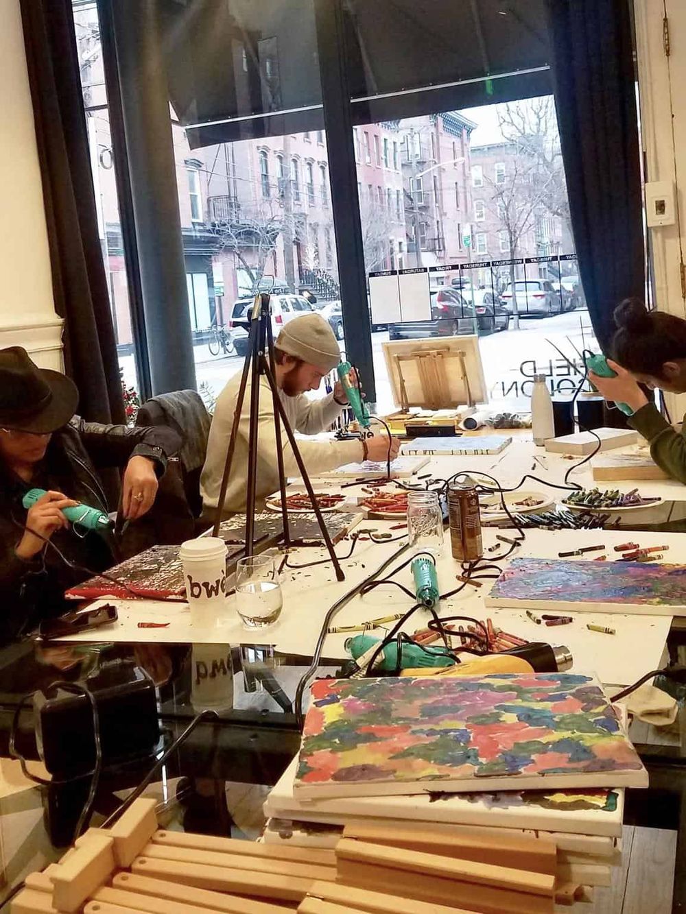 Colorful art workshop with participants creating jewelry and paintings in a bright, cozy studio.