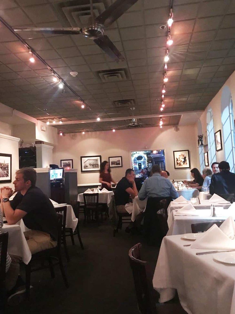 Cozy upscale restaurant interior with white tablecloths, framed wall art, and warm ambient lighting, perfect for fine dining experiences.