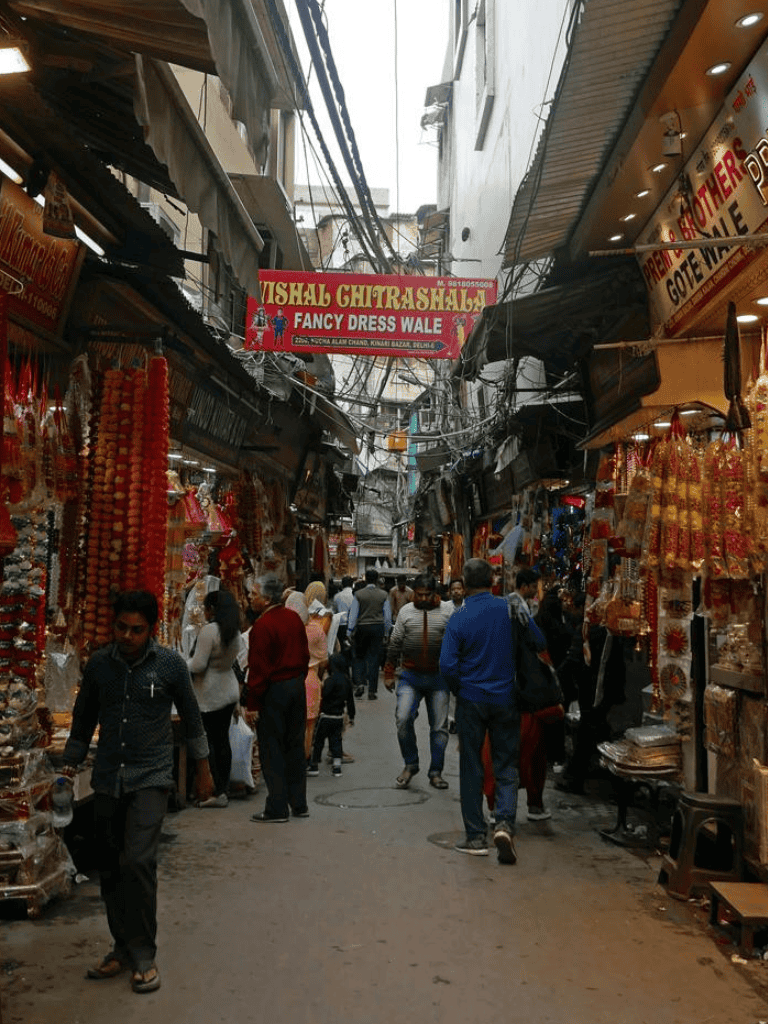 Colorful marketplace street in Delhi with clothing and jewelry shops bustling with shoppers.