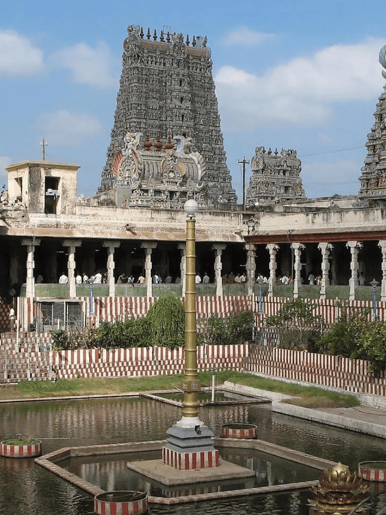 Ancient South Indian temple gopuram with intricate carvings, surrounded by water features and lush greenery.