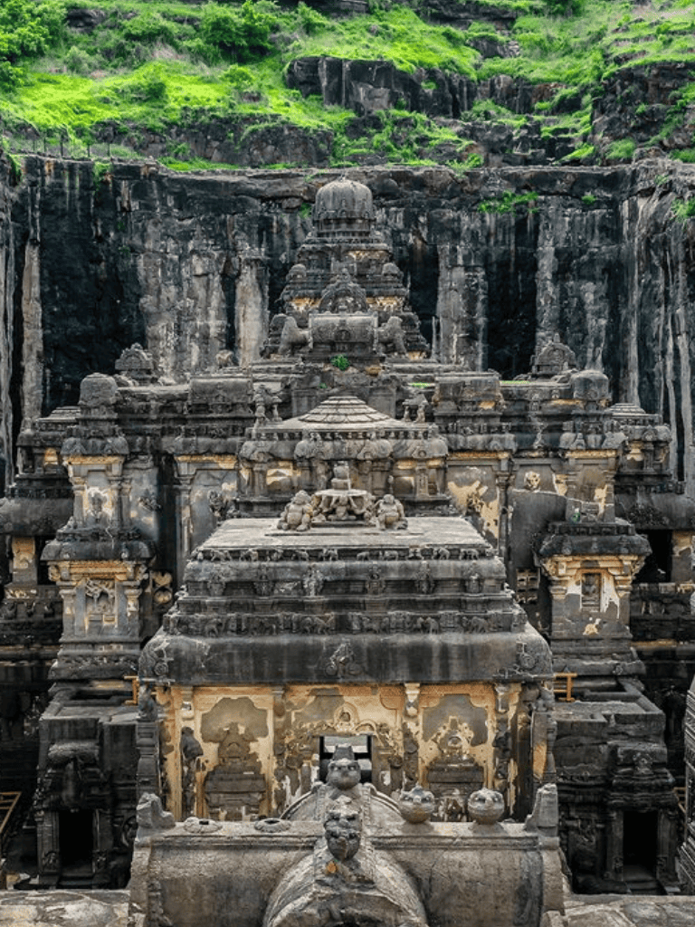 Ancient rock-cut temple with intricate carvings, steep hillside with lush greenery in the background.