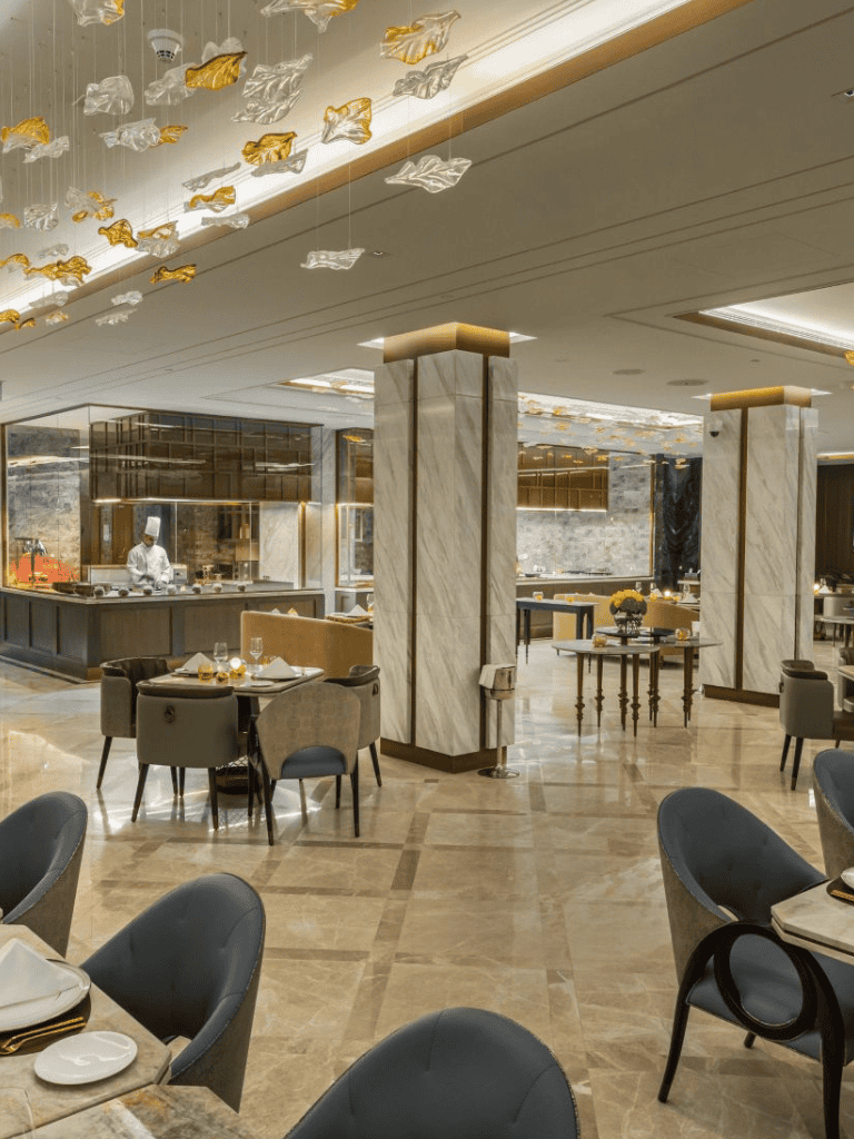 Elegant hotel restaurant featuring modern decor and a chef preparing dishes in a luxurious setting.