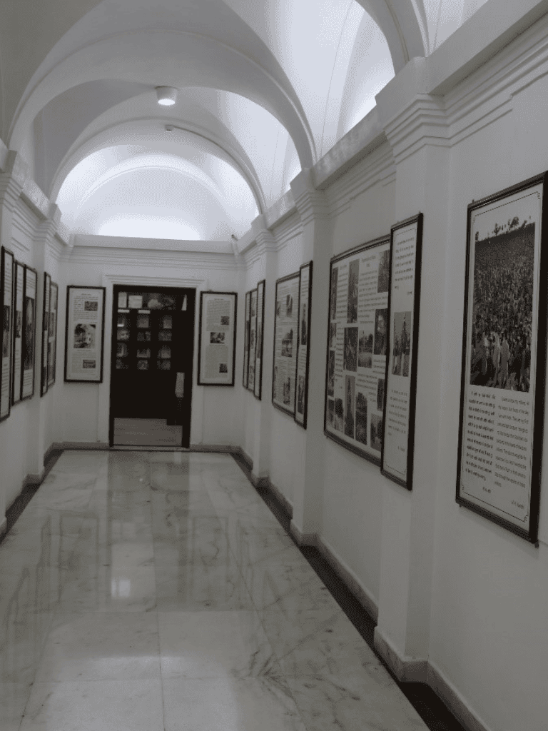 Historical museum exhibit with framed photographs and informational panels, white arched ceilings, marble flooring.