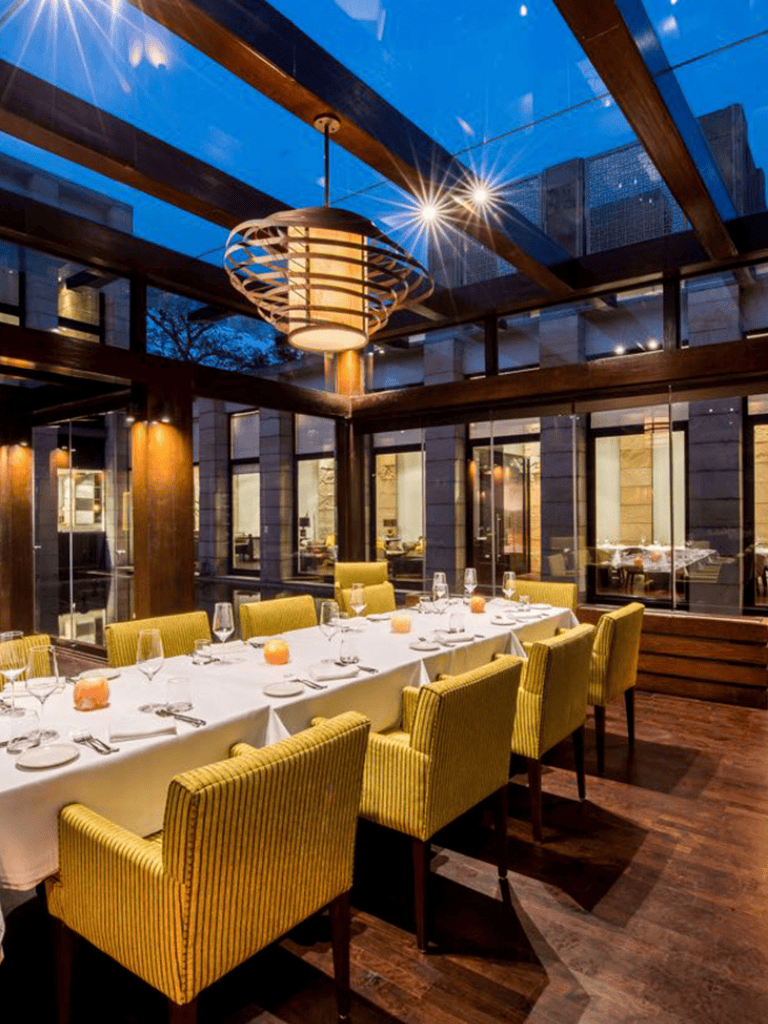 Elegant restaurant interior with yellow upholstered chairs, glass walls, and warm lighting for fine dining.