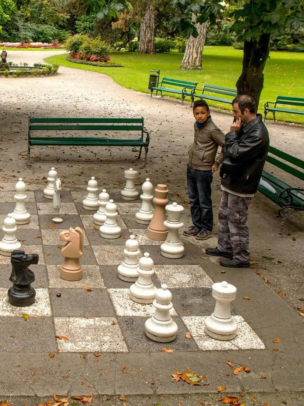 Large outdoor chess set in a scenic park with parents and children playing chess.