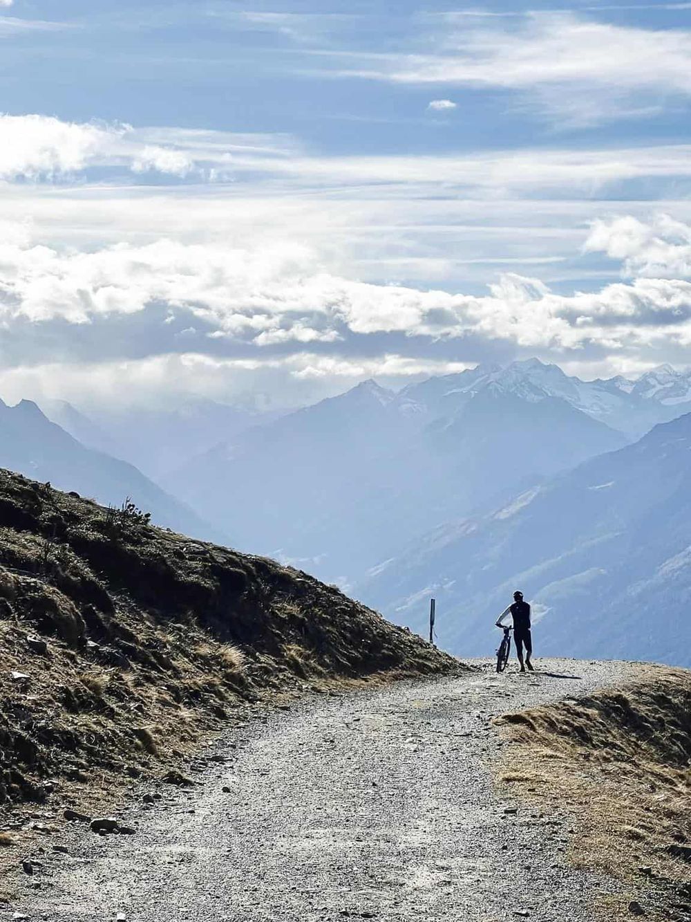Scenic mountain trail with cyclist enjoying a panoramic view of the mountains and sky.
