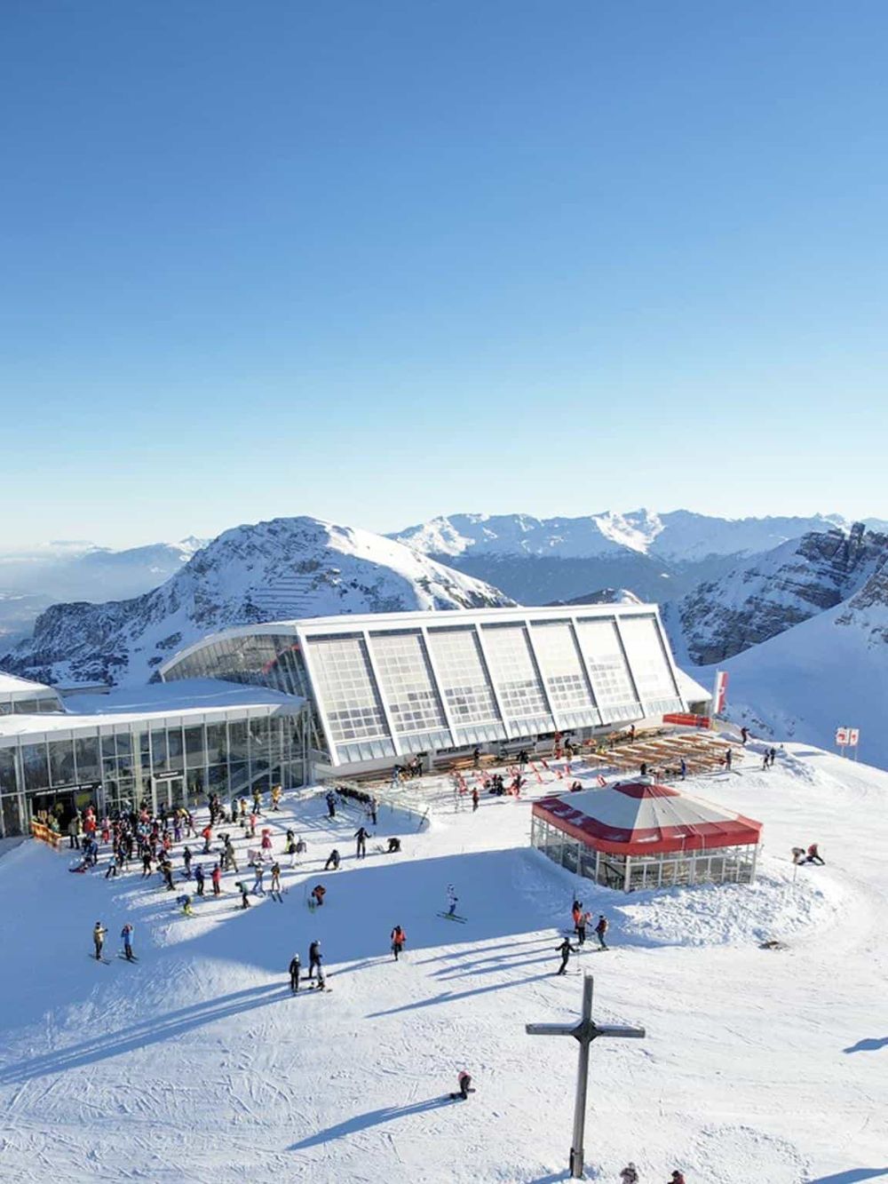 Modern ski resort building with large glass windows and snow-covered mountains in the background.