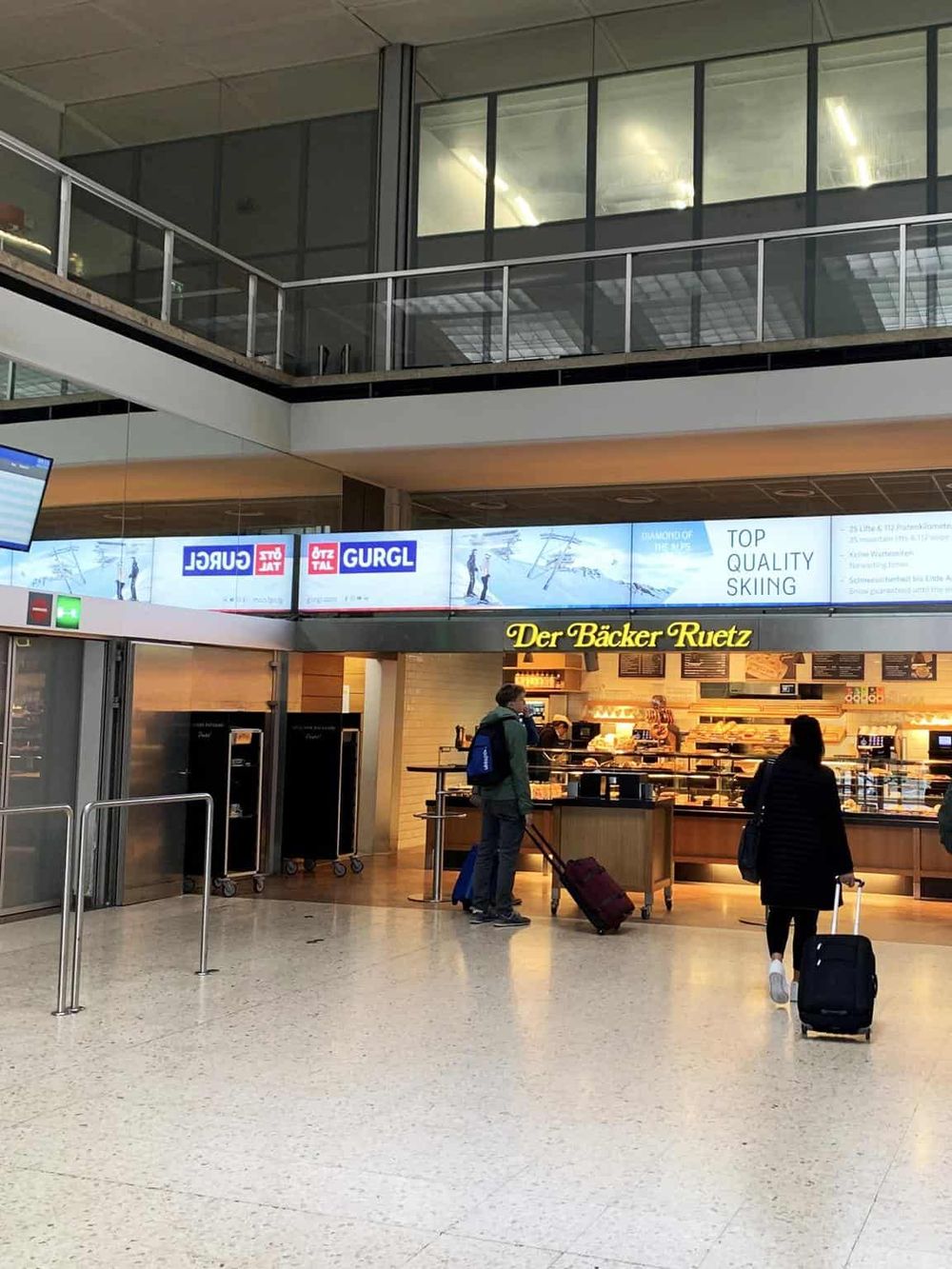 Bright airport terminal with travelers, bakery shop, digital signage, and modern architecture.