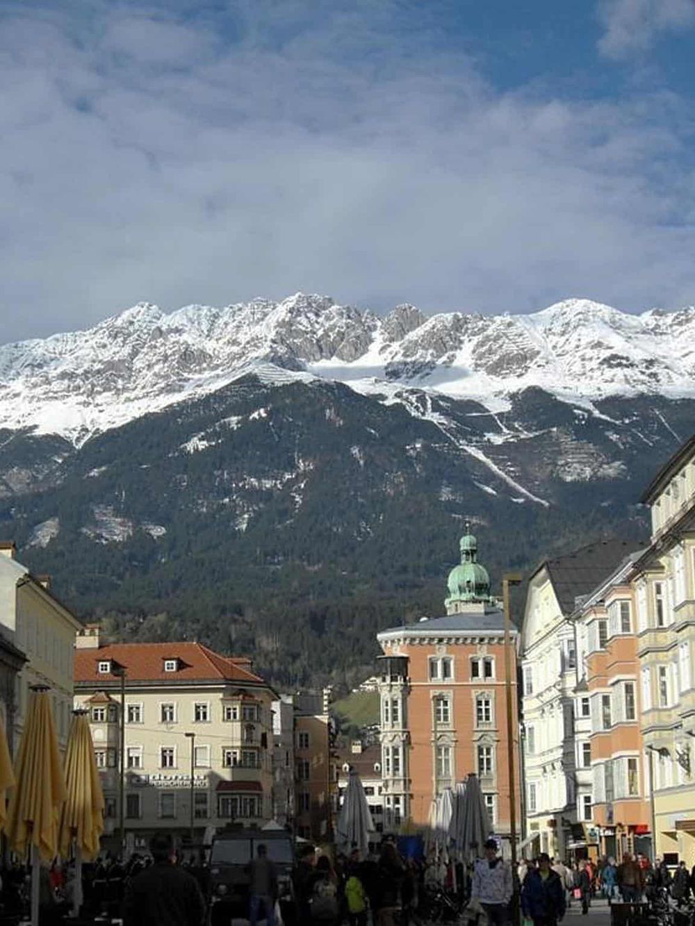 Snow-capped mountains in Innsbruck, Austria, with a lively city square and historic architecture.