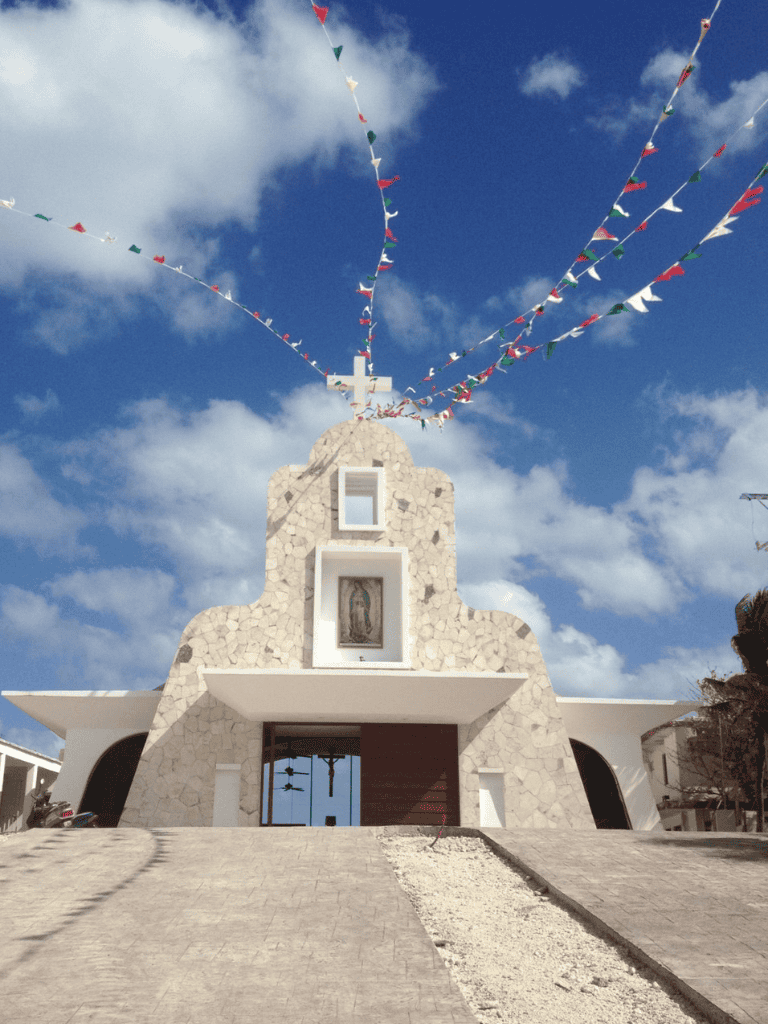 Colorful religious banners flying over a modern church with stone exterior and a cross at the top.