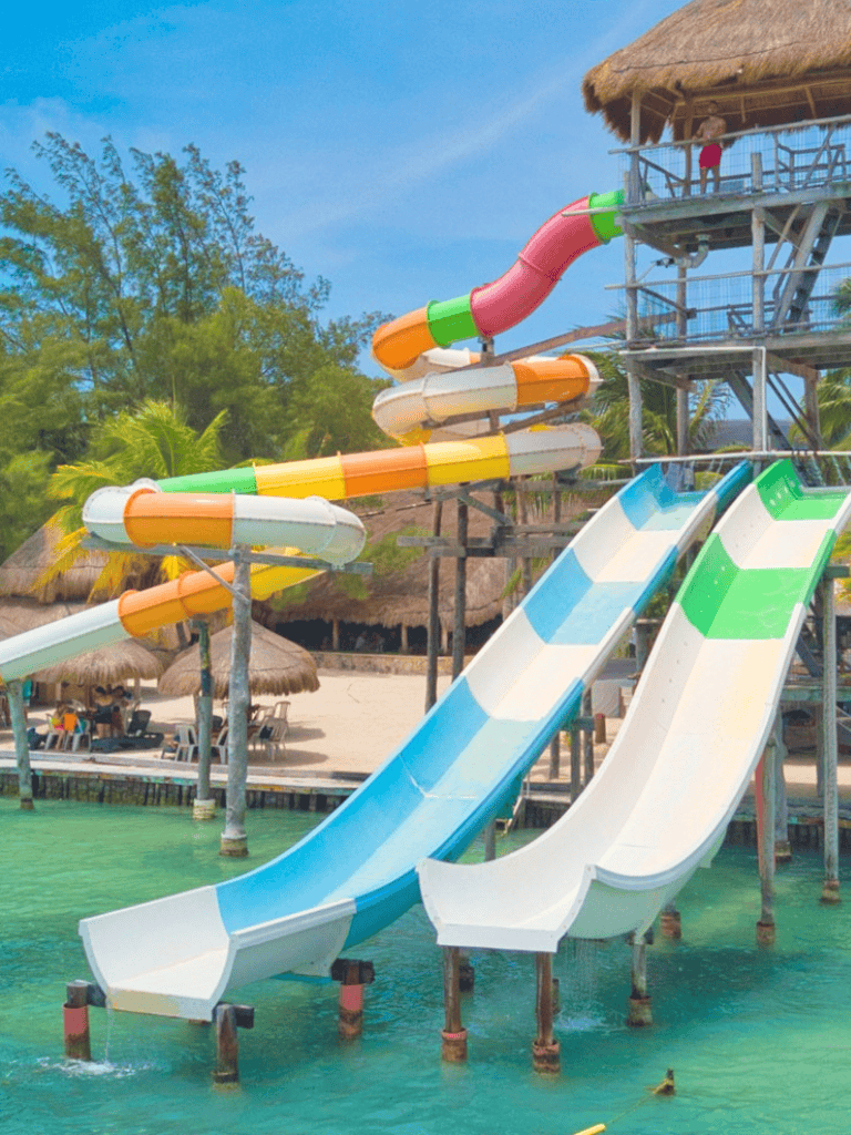 Colorful water slides at tropical water park with thatched huts and lush greenery.