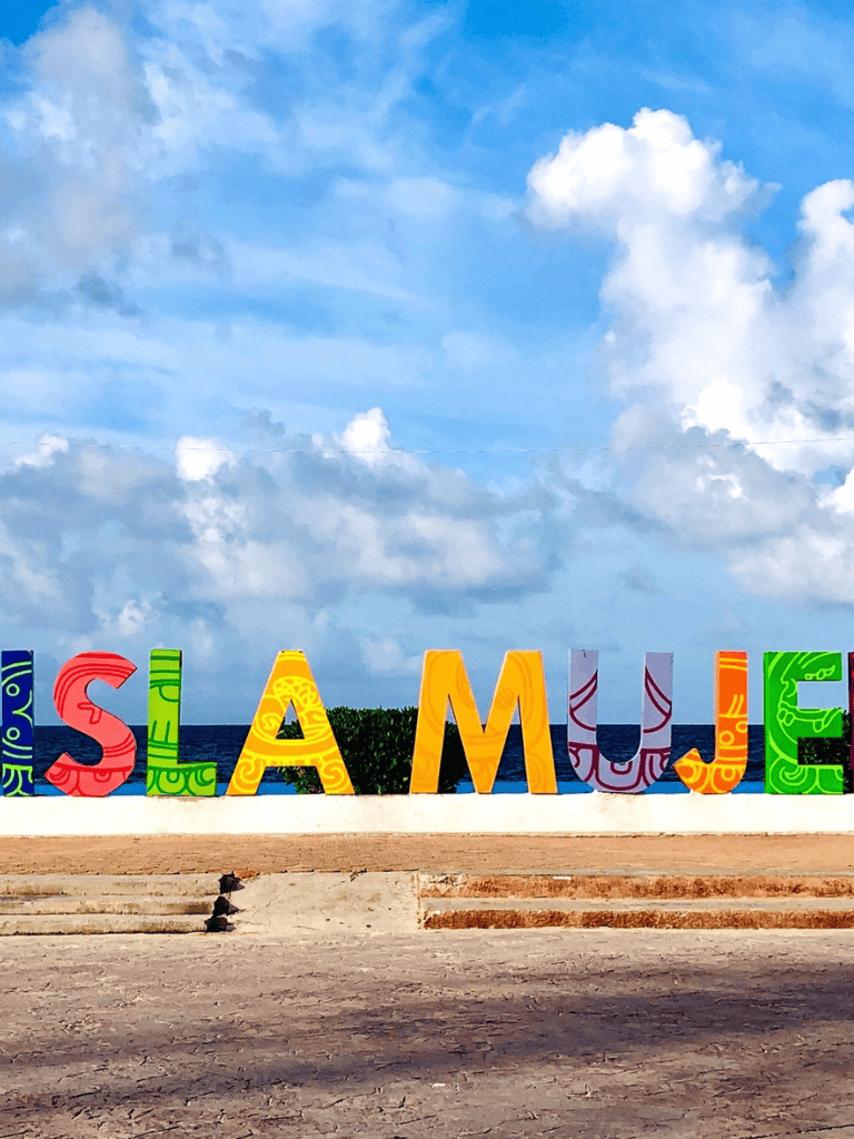 Colorful outdoor "Welcome to Cancun" sign on beach with blue sky and clouds, tourist photo for vacation destination.