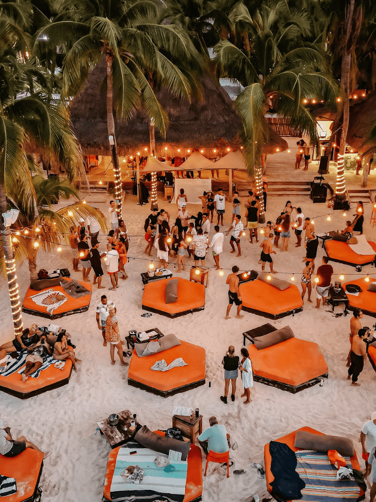 Relaxing beach party at tropical resort with tents, cozy lounges, and palm trees.