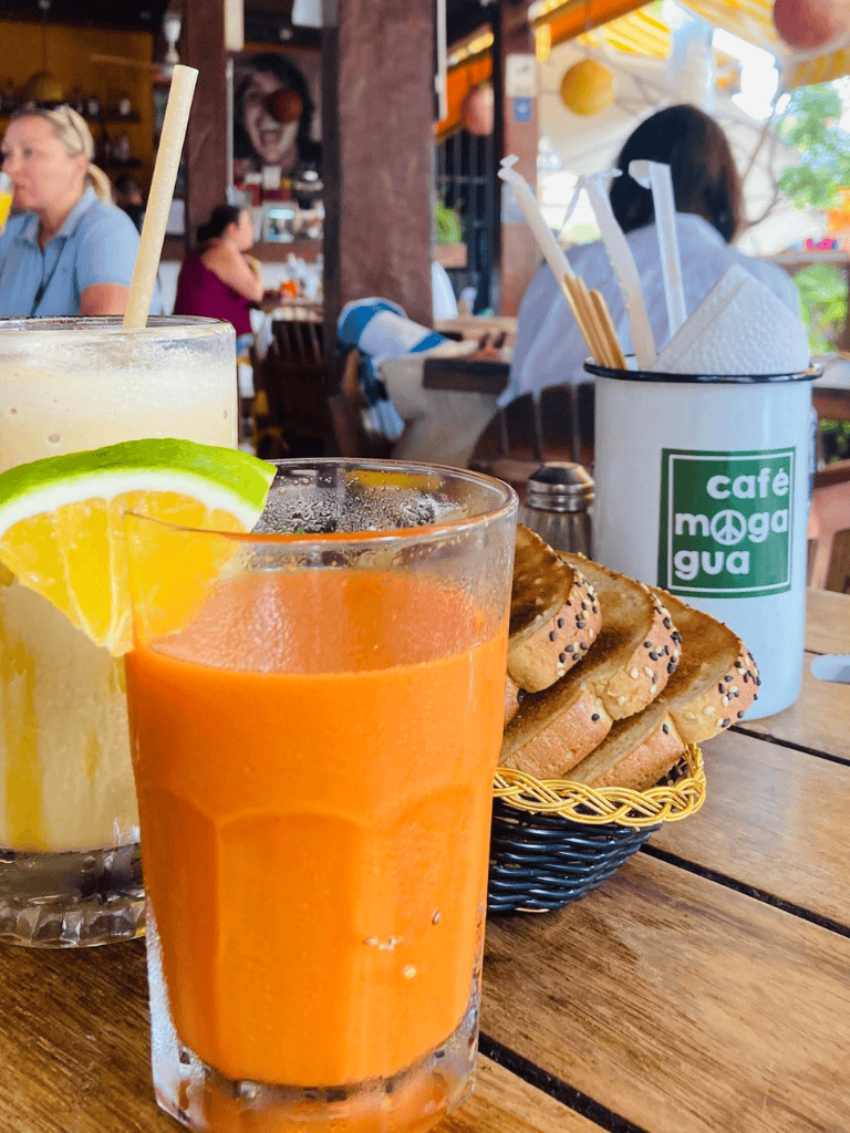 Refreshing fruit juice served with lemon wedge at Cafe Moga Gua, outdoor dining with bread basket on wooden table.