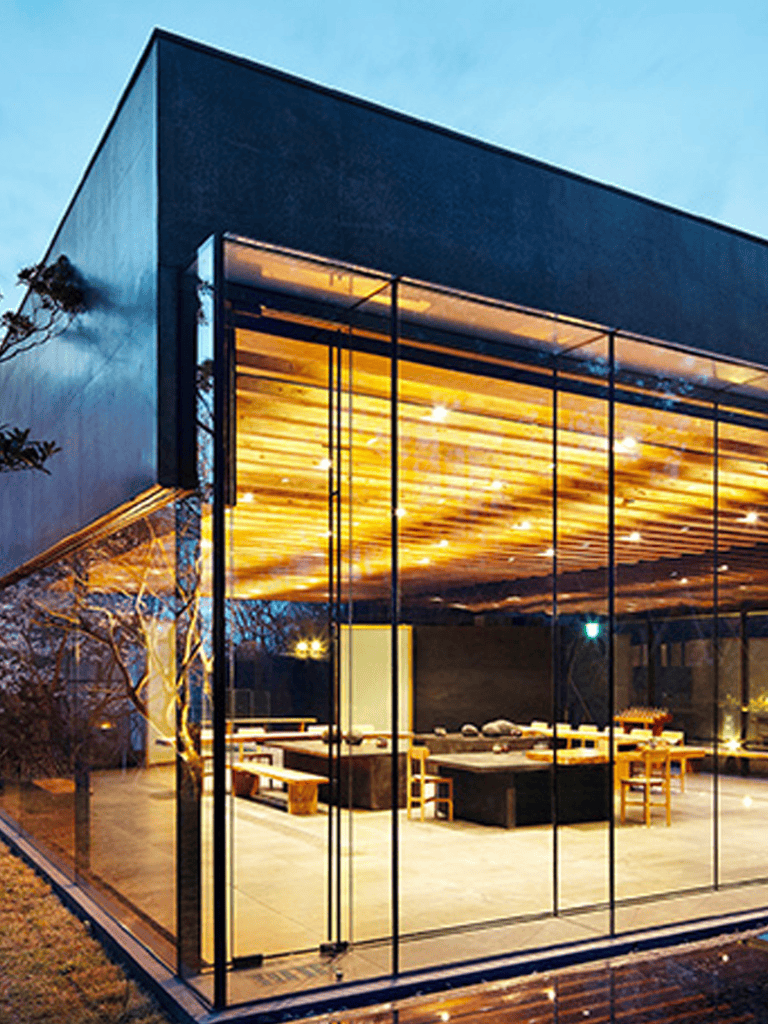 Modern glass building with illuminated interior, stylish design, and scenic outdoor setting.