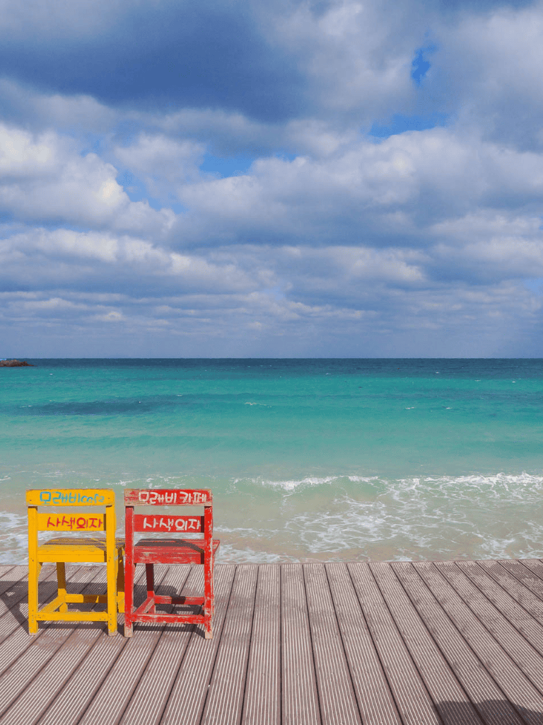 Colorful beach chairs on wooden deck facing turquoise ocean under cloudy sky, offering scenic seaside relaxation at QuestForDirections.